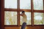 Person in T-Shirt öffnet ein Fenster in einem Holzraum