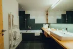 modernes Badezimmer mit Badewanne, Waschbecken und grünen Schränken