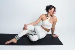 Frau in Yogapose auf einer schwarzen Matte vor weißem Hintergrund