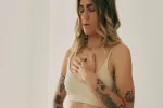 Person mit Tattoos in hellem Top, Hand auf der Brust