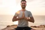 Mann praktiziert Yoga am Meer bei Sonnenuntergang