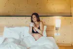 Eine Person sitzt auf einem Bett mit weißen Laken in einem warm beleuchteten Raum