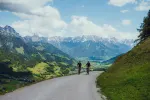 Zwei Radfahrer auf einer kurvenreichen Straße mit Bergen im Hintergrund