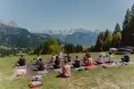 Gruppe sitzt auf Gras mit Bergen im Hintergrund