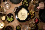 Ein Tisch mit Käsefondue und verschiedenen Beilagen.