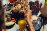 Tisch mit verschiedenen Speisen und Getränken, Hand greift nach Brot.