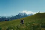 Zwei Personen gehen in einer bergigen Landschaft mit grünen Wiesen