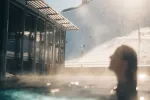 Person im Wasser mit Gebäude und Bergen im Hintergrund