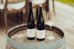 Zwei Weinflaschen und ein Glas auf einem Holztischfass