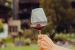 Hand hält ein Glas Rotwein im Freien