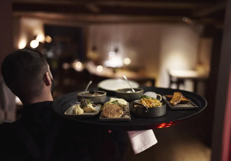 Kellner trägt einen Tablett mit verschiedenen Speisen im Restaurant.