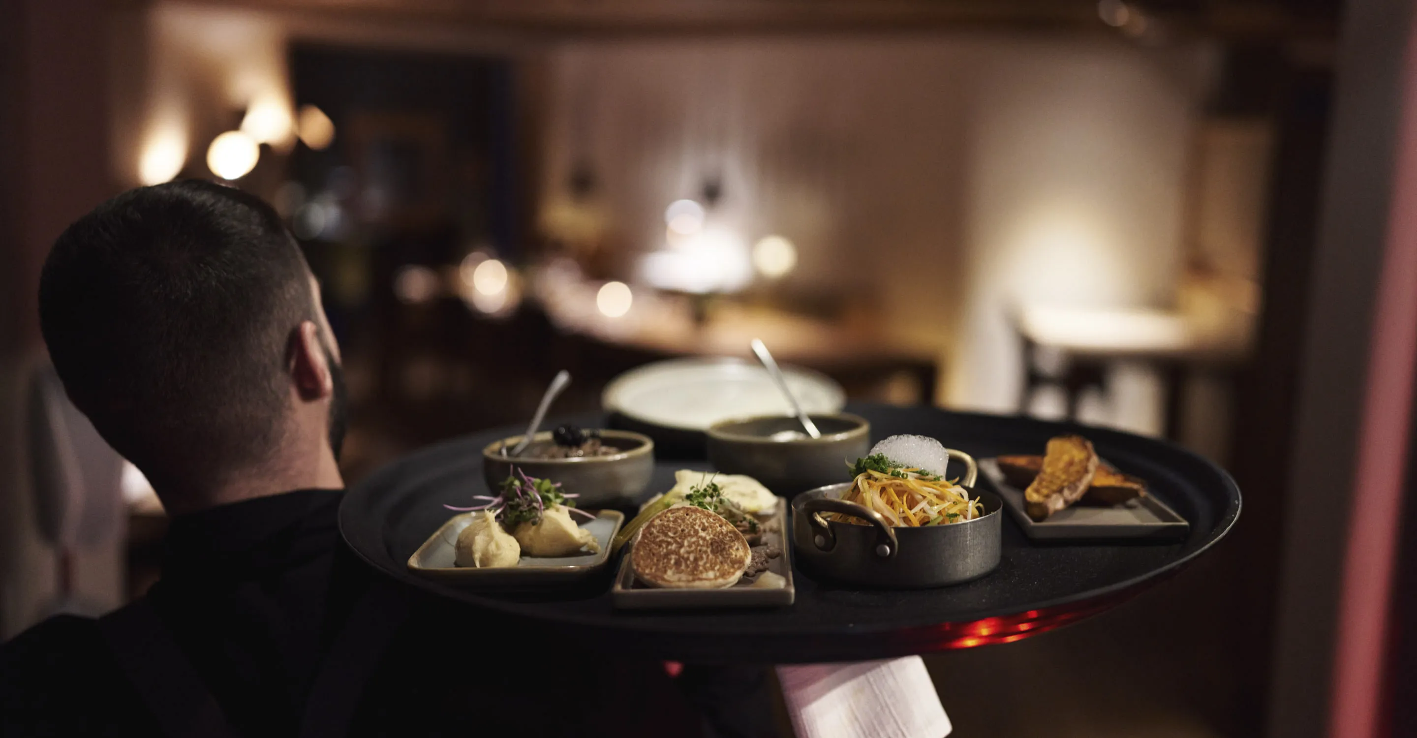 Kellner trägt eine Platte mit verschiedenen Speisen im Holzhotel Forsthofalm.