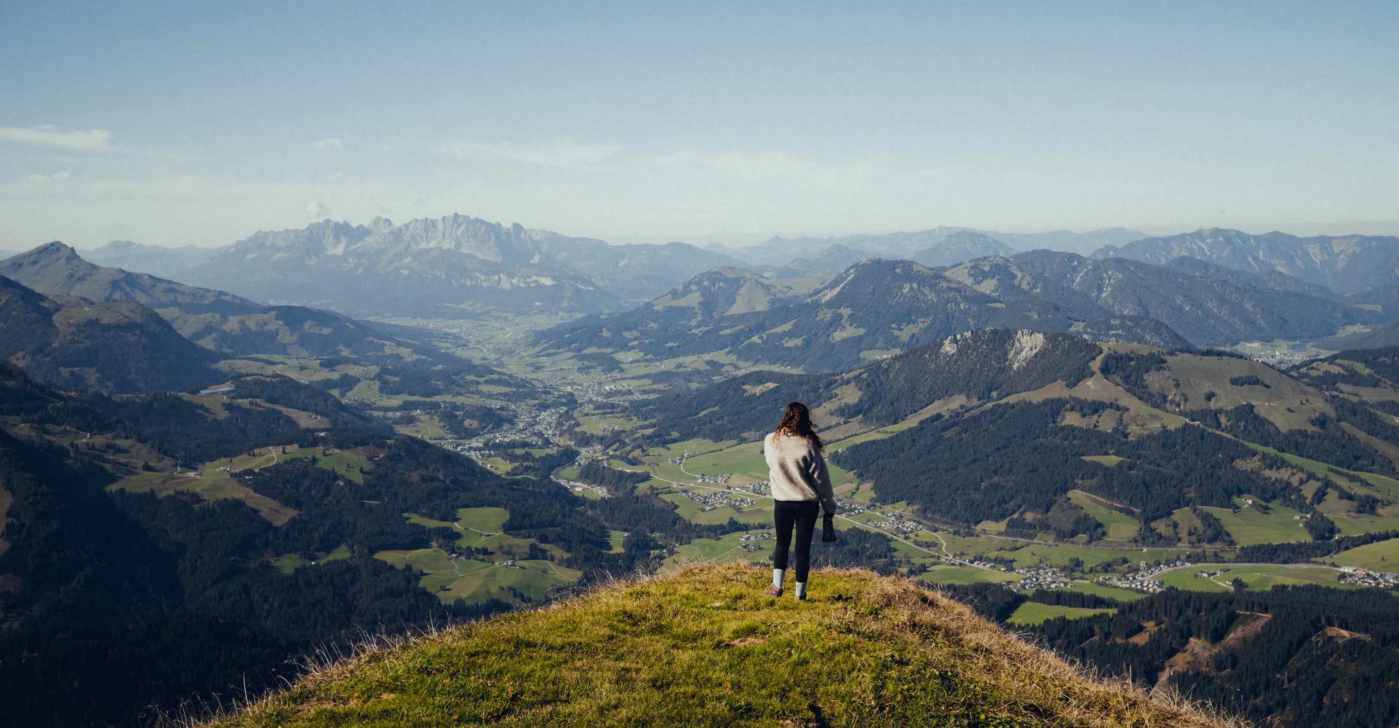 Frau steht auf einem Hügel mit Blick auf die Berge und Täler.