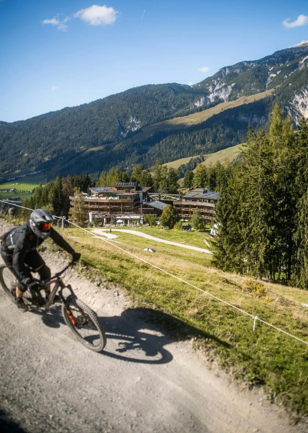 Fahrer auf einem Mountainbike in einer bergigen Landschaft mit Bäumen und Gebäuden.