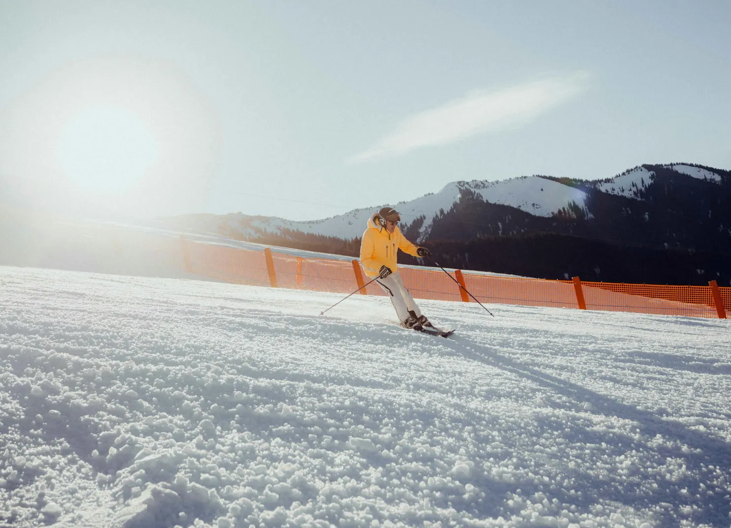 Skifahrer in gelber Jacke auf einer verschneiten Piste mit Bergen im Hintergrund