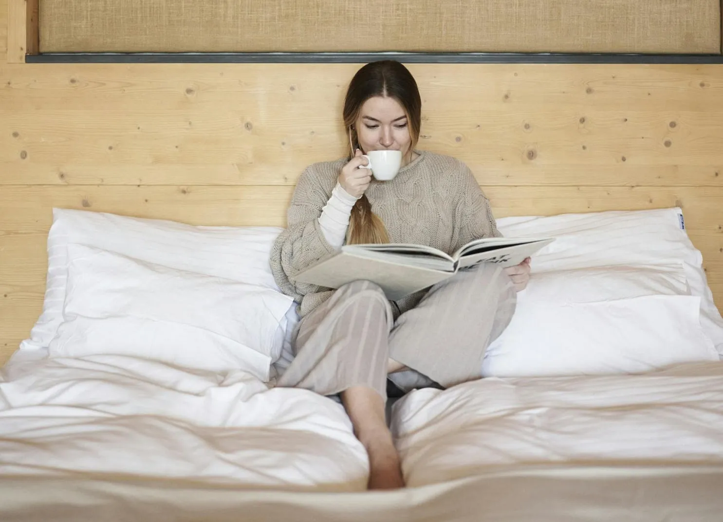 Frau auf dem Bett, liest ein Buch und hält eine Tasse.