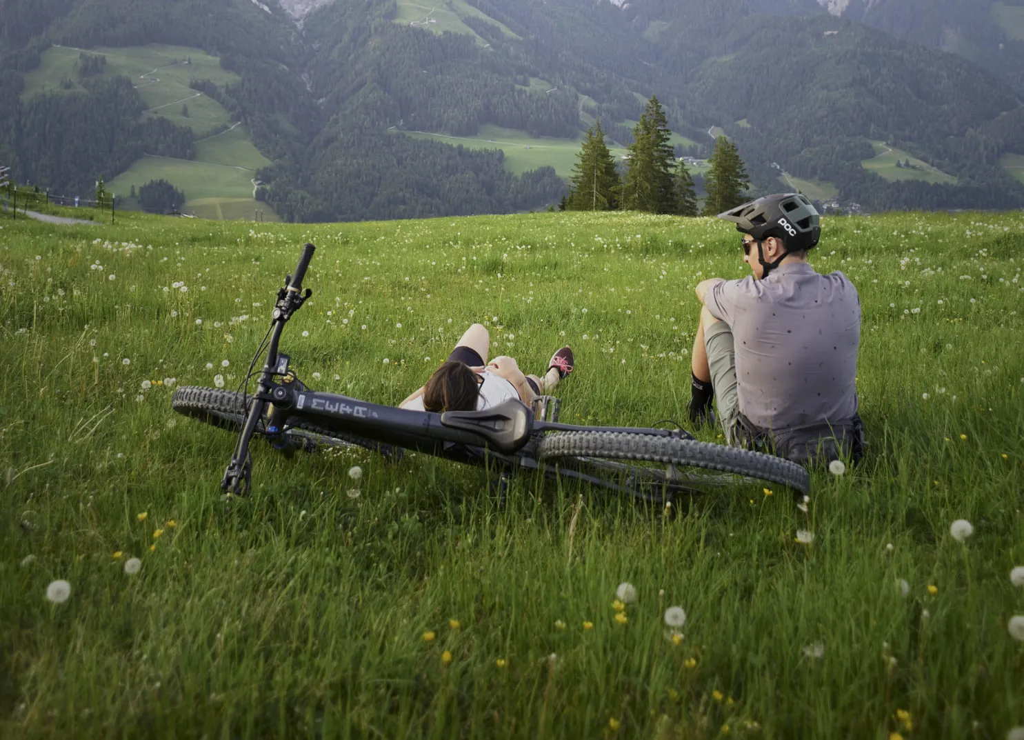 Zwei Personen auf einer Wiese in Leogang, ein Fahrrad liegt daneben.