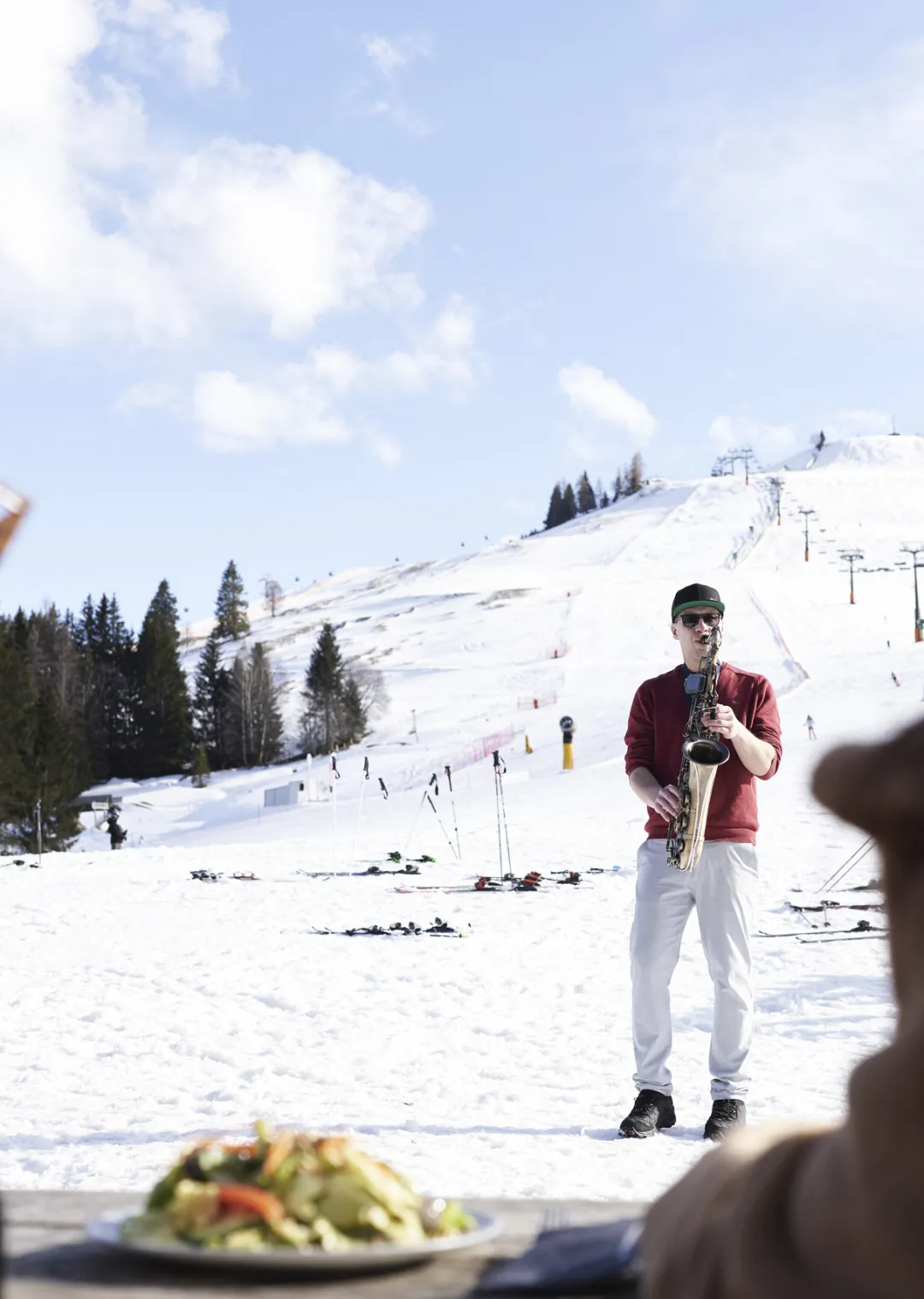 Saxophonist auf verschneitert Skihang in Leogang, im Hintergrund Skilifte.
