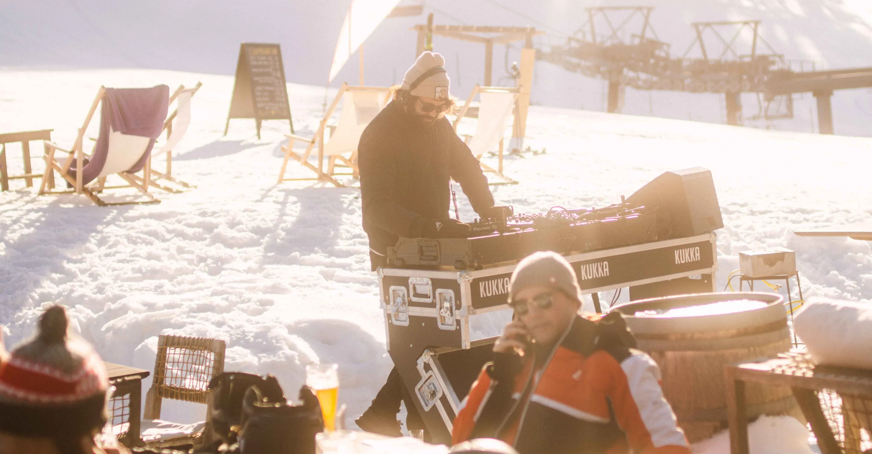 DJ steht auf einer Terrasse im Schnee mit Musikanlage und Gästen
