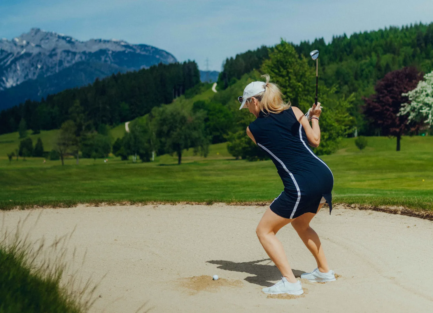 Frau im Golfkleid schlägt aus dem Sandbunker, Berge im Hintergrund