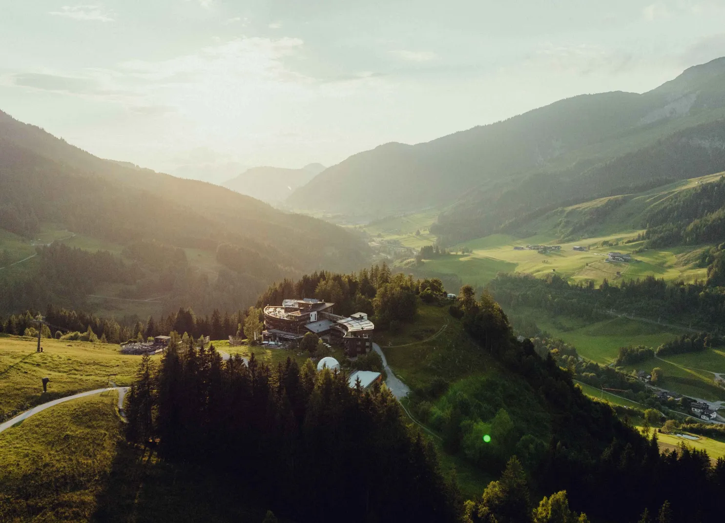 Aussicht auf Berge und Täler bei Sonnenuntergang, mit Gebäuden in der Nähe.