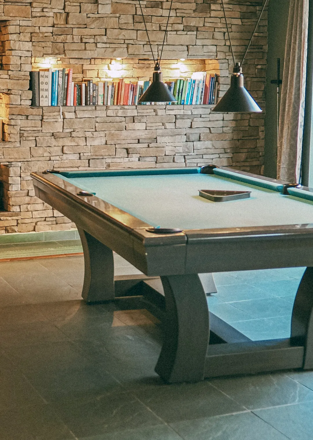 Billardtisch vor einer Steinwand mit Bücherregalen
