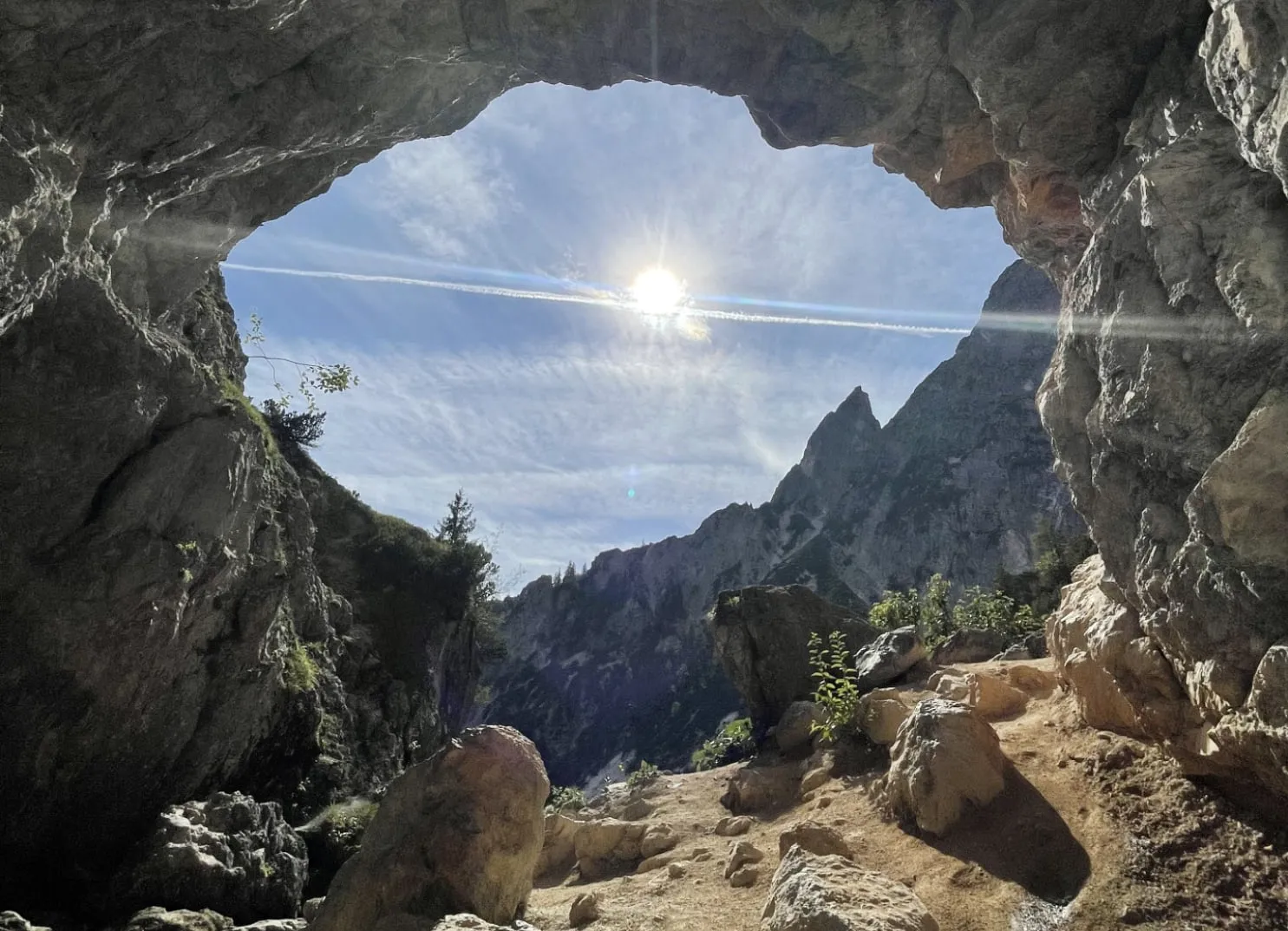 Blick durch einen felsigen Bogen mit Sonne und Bergen im Hintergrund